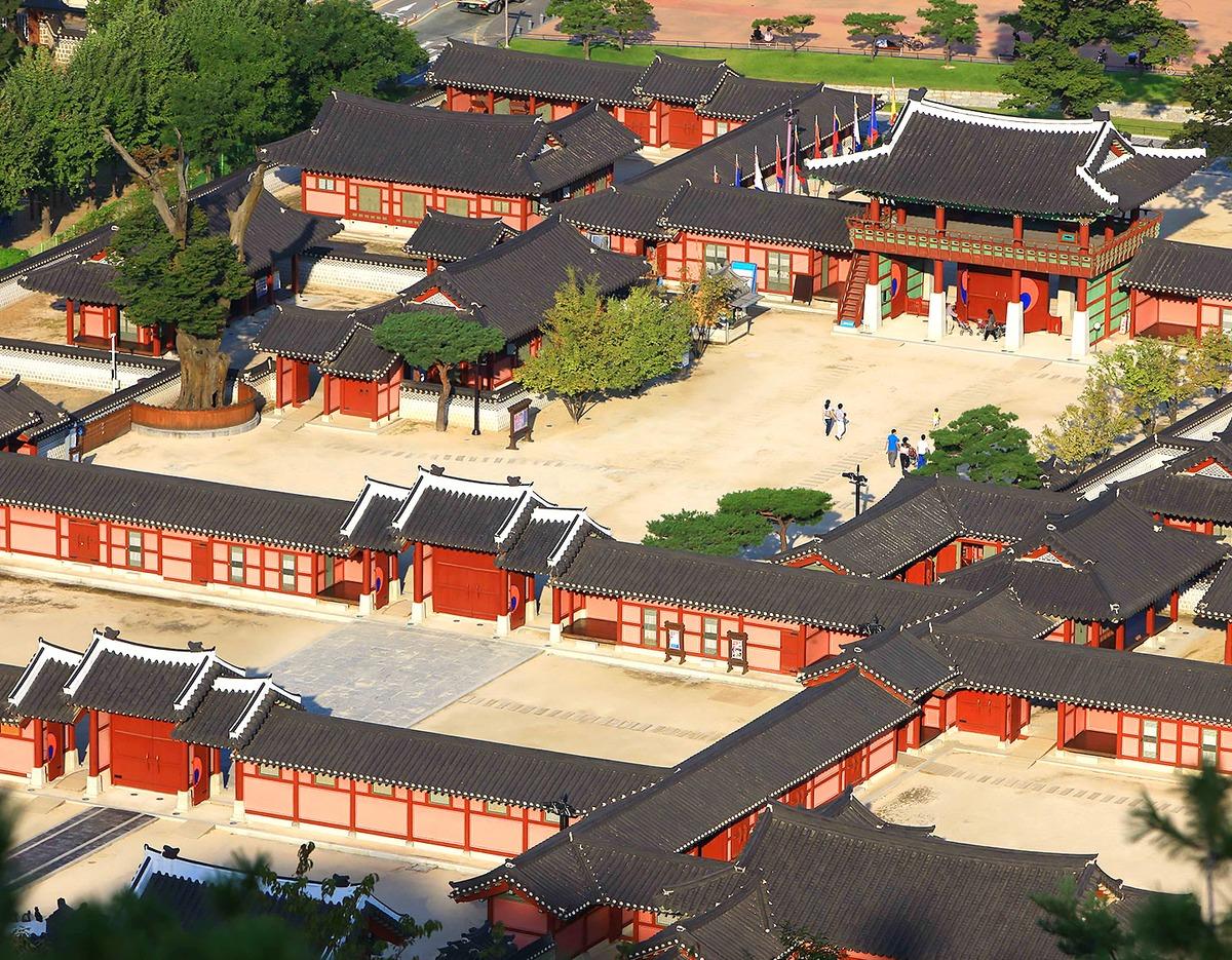 Aerial view of Hwaseong Haenggung Palace courtyard and red wooden buildings with dark tiled roofs and visitors walking around