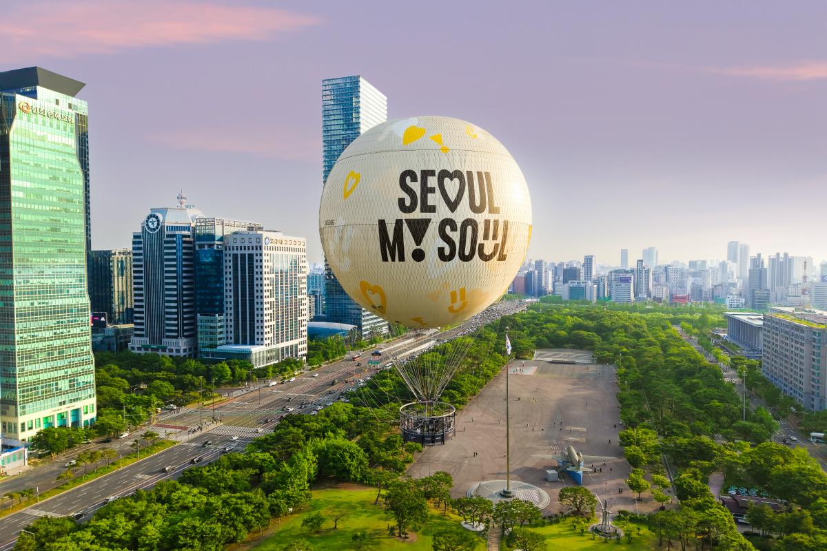 Large tethered helium balloon reading "Seoul My Soul" floating over Yeouido park with surrounding skyscrapers and tree-lined roads