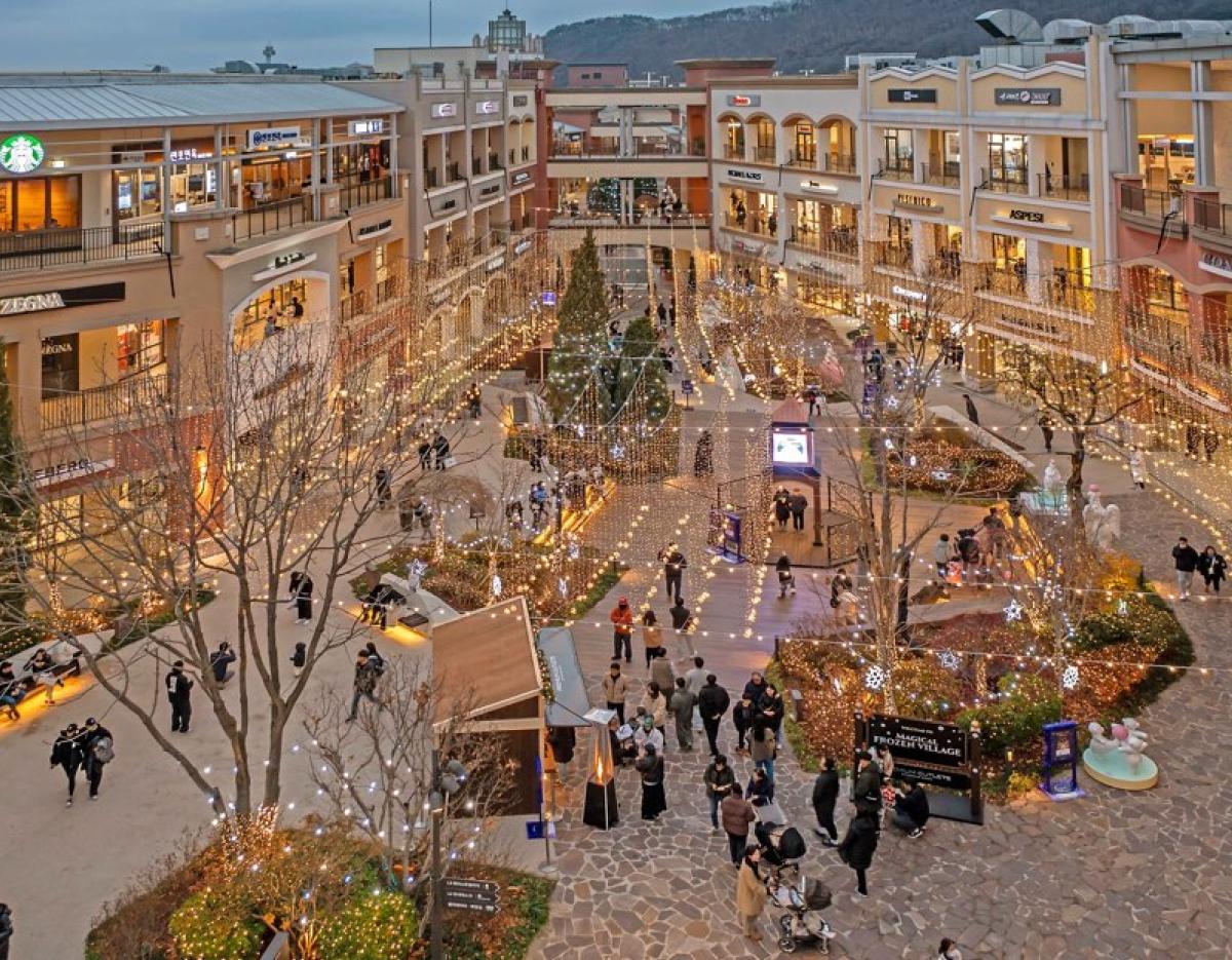 Paju Premium Outlet open-air shopping plaza at dusk with string lights, decorated trees and shoppers strolling between stores