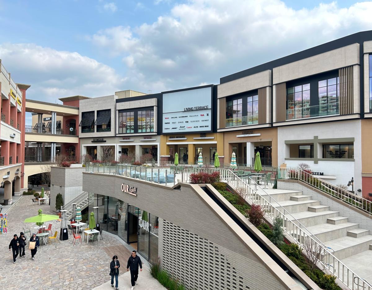 Outdoor courtyard of Paju Premium Outlet with shops, terrace seating, staircases and shoppers walking on stone pavement