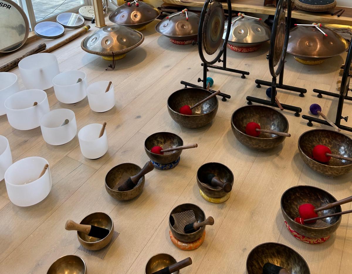 Assorted singing bowls, crystal bowls, gongs and mallets arranged on a wooden floor for a sound bath meditation session