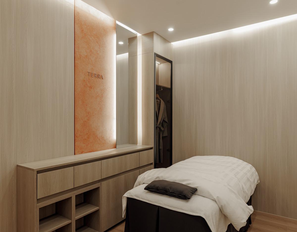 Minimalist treatment room at Terra clinic with a padded treatment bed, wooden cabinetry, soft lighting, and robe closet.