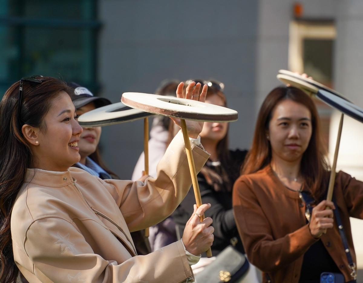 Visitors practicing traditional Korean hand drum spinning on small round drums held on sticks at a cultural workshop