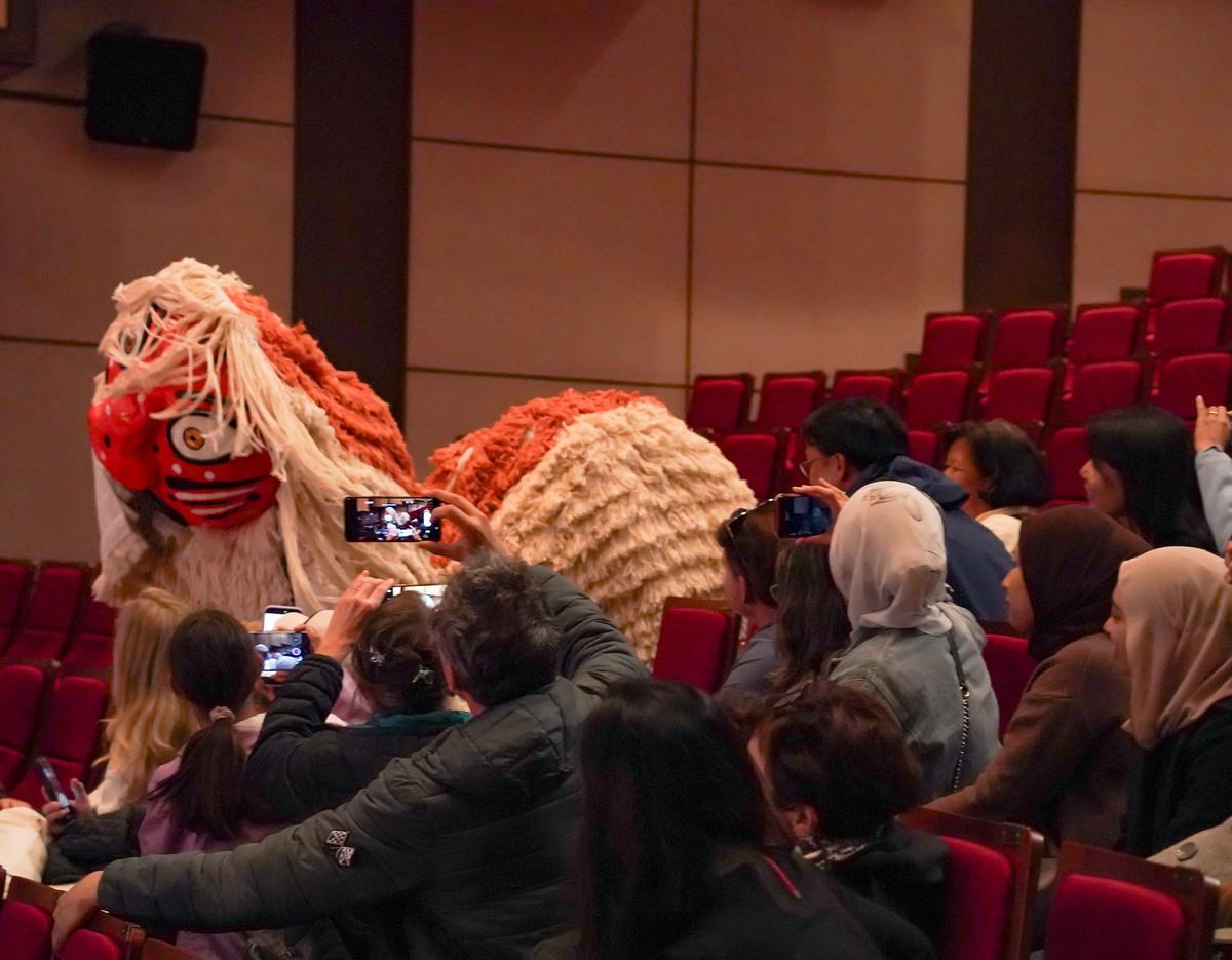 audience photographing a large traditional Korean lion mask costume weaving through red theater seats during performance
