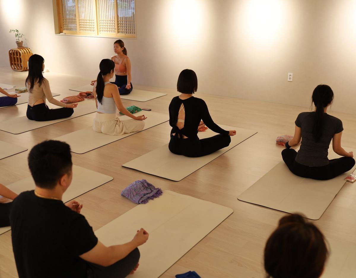 small group seated cross-legged on yoga mats in a softly lit studio practicing guided meditation near Gwangalli Beach