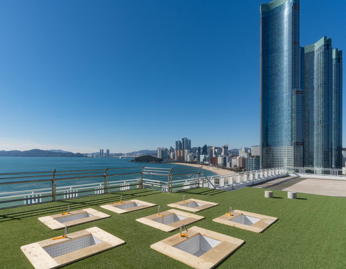 HillSpa rooftop outdoor foot baths on artificial turf with ocean view and Haeundae skyline in background