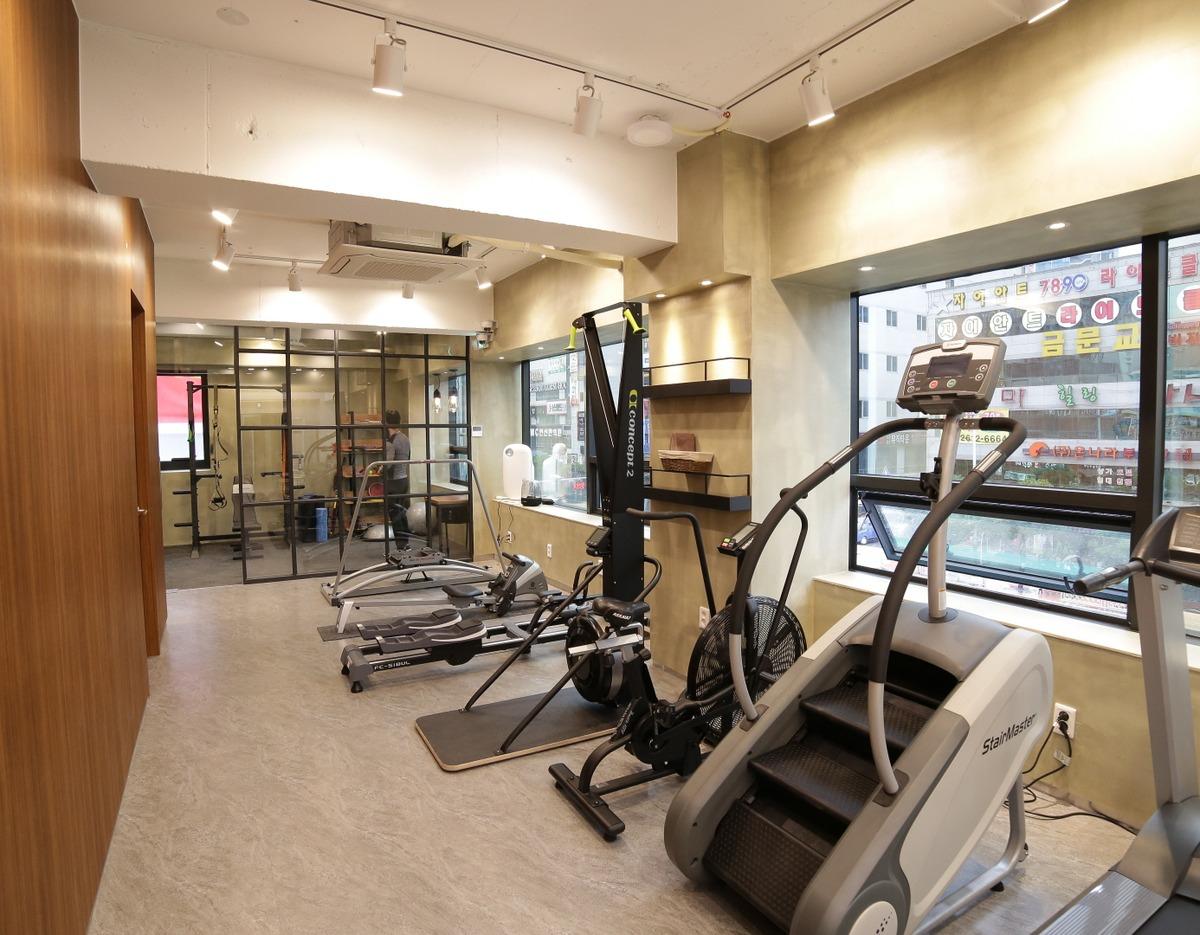 Bright modern clinic workout room with stair climber, rowing machines, cardio equipment and glass-walled training area next to windows