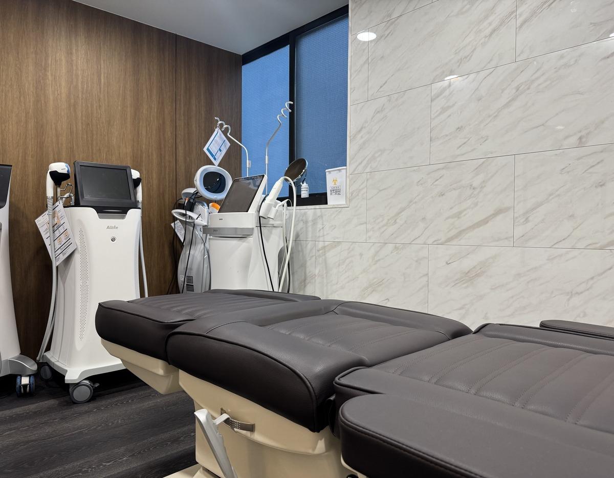 Treatment room with reclining black leather spa bed and white skin‑care machines against wood and tile walls
