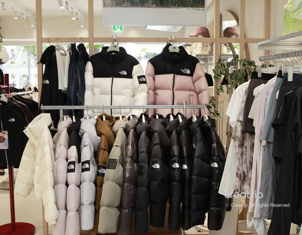 Rack of The North Face puffer jackets in various colors (white, pink, beige, brown, black) displayed inside Hanam premium store