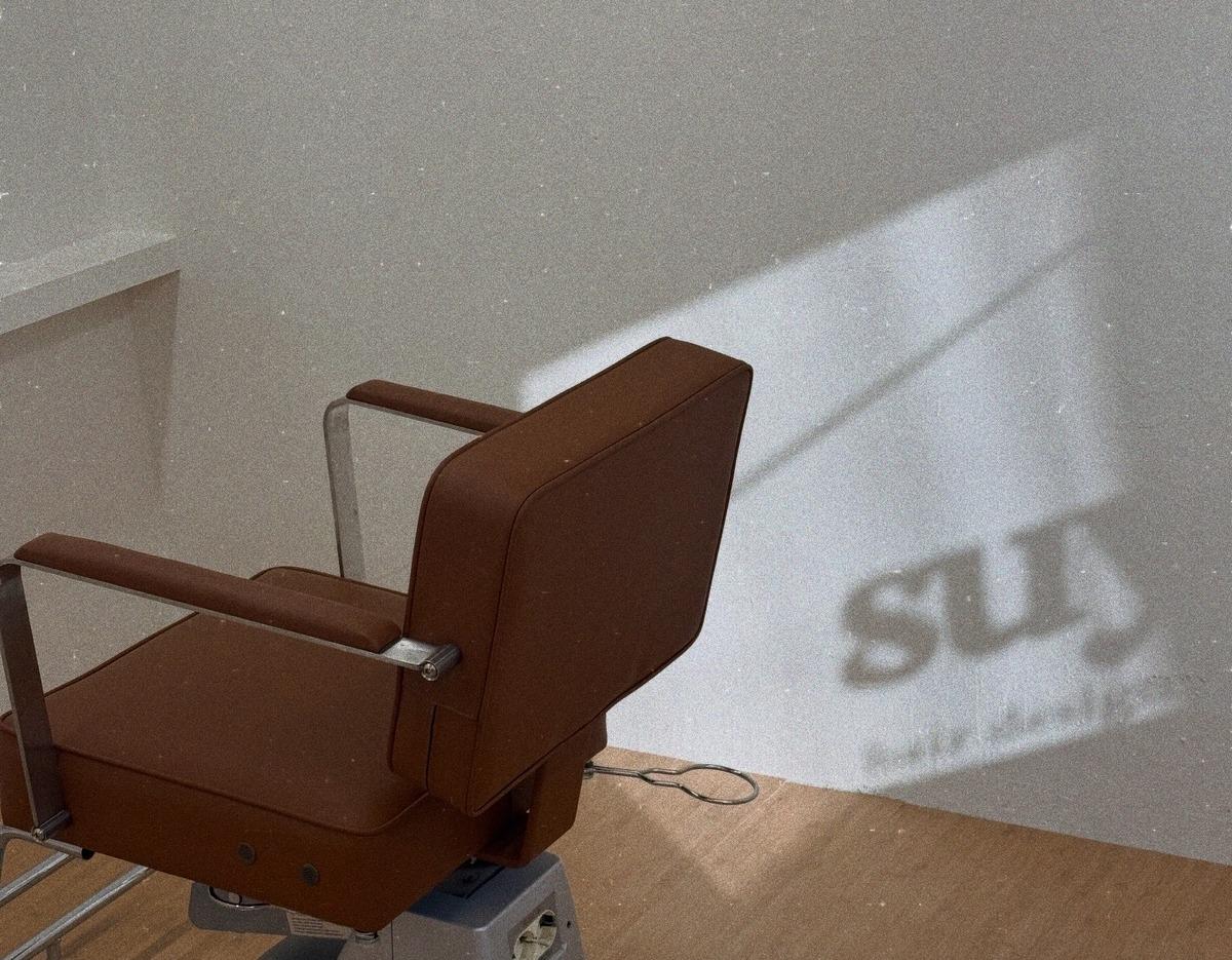스위브 salon interior showing a brown vintage-style barber chair casting a soft shadow on a white wall