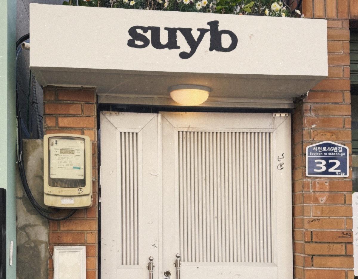 suyb salon entrance with white ribbed double doors, small awning sign reading "suyb" and address plaque 32
