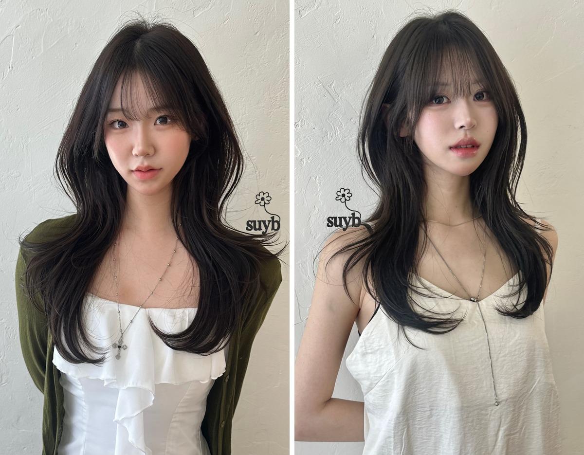 long layered dark brown haircut with face-framing bangs on two models wearing white tops, salon logo "suyb" on wall