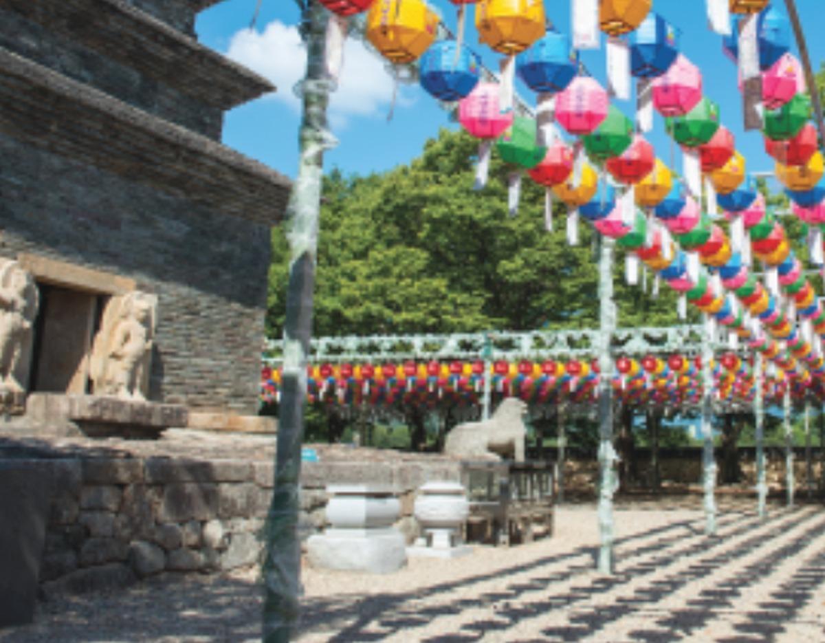 Bulguksa temple courtyard with stone pagoda, guardian lion sculptures and rows of colorful hanging lanterns under blue sky