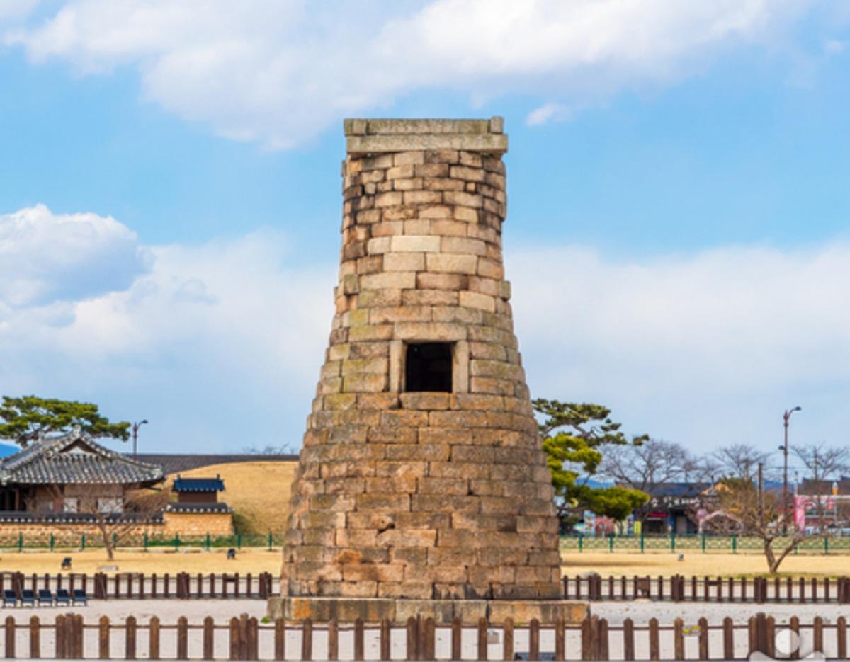 Cheomseongdae stone astronomical observatory tower standing on grassy grounds with traditional hanok buildings behind