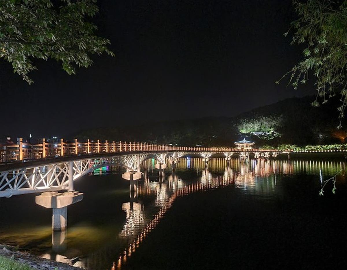 Moonlit wooden Moonlight Bridge (Wolyeonggyo) lit up at night with string lights reflecting on calm river in Andong.