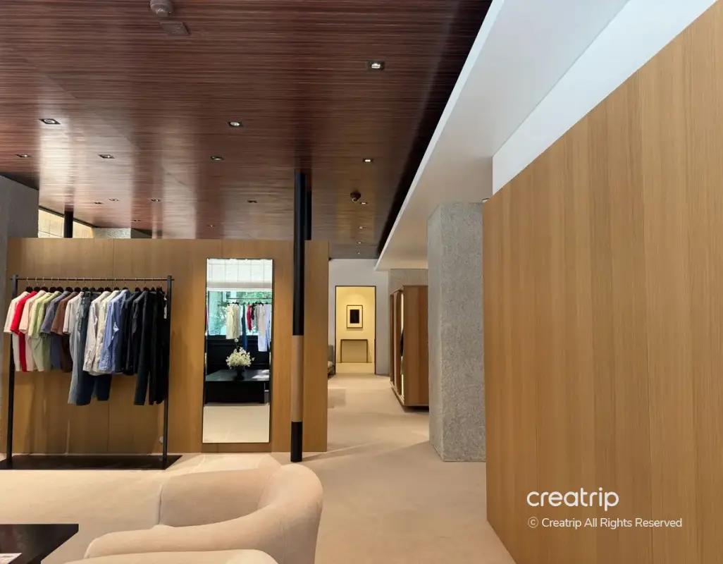 Minimal menswear boutique interior with wooden panels, clothing rack, full-length mirror, beige sofa and recessed ceiling lights