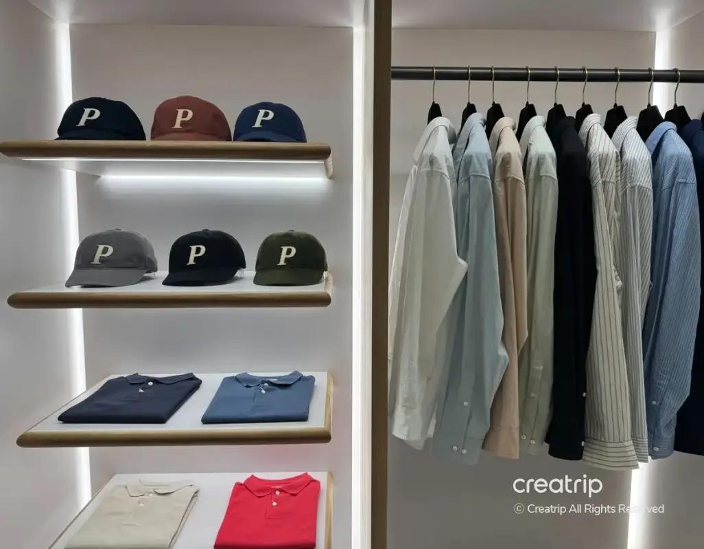 Pottery Seongsu display of folded polos and caps with "P" logo on illuminated shelves beside a rack of neutral button-down shirts