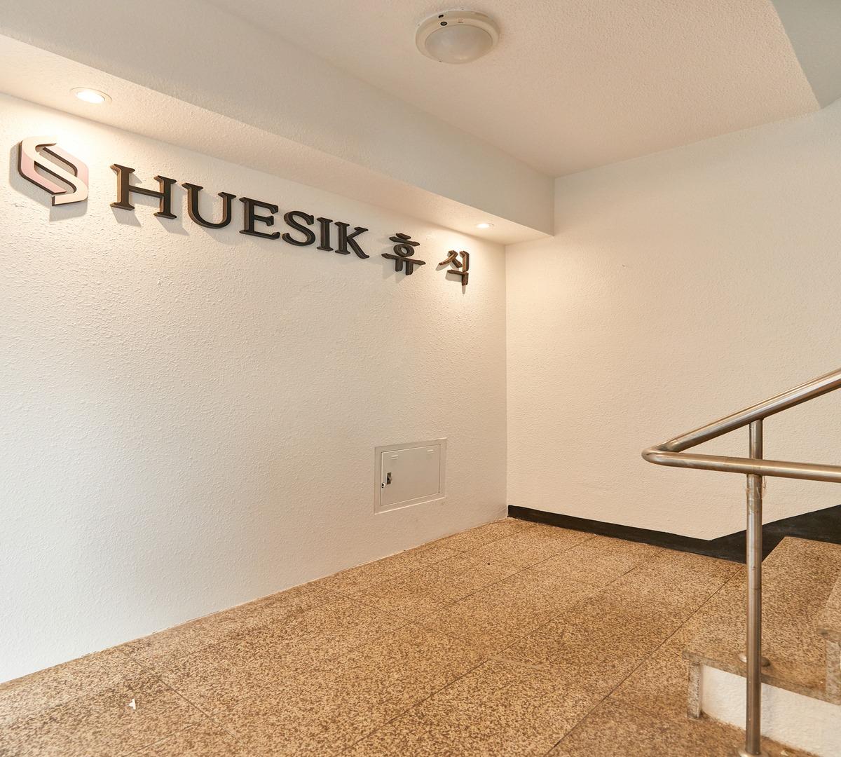 HUESIK 휴식 metal wall sign above tiled stair landing with stainless handrail and recessed ceiling lights