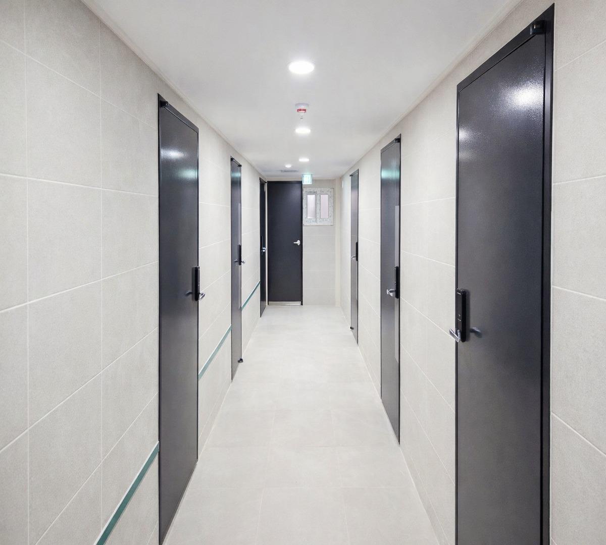 Hallway with tiled walls and floor lined with multiple dark gray individual room doors at HUESIK DAERIM (휴식 대림역점).