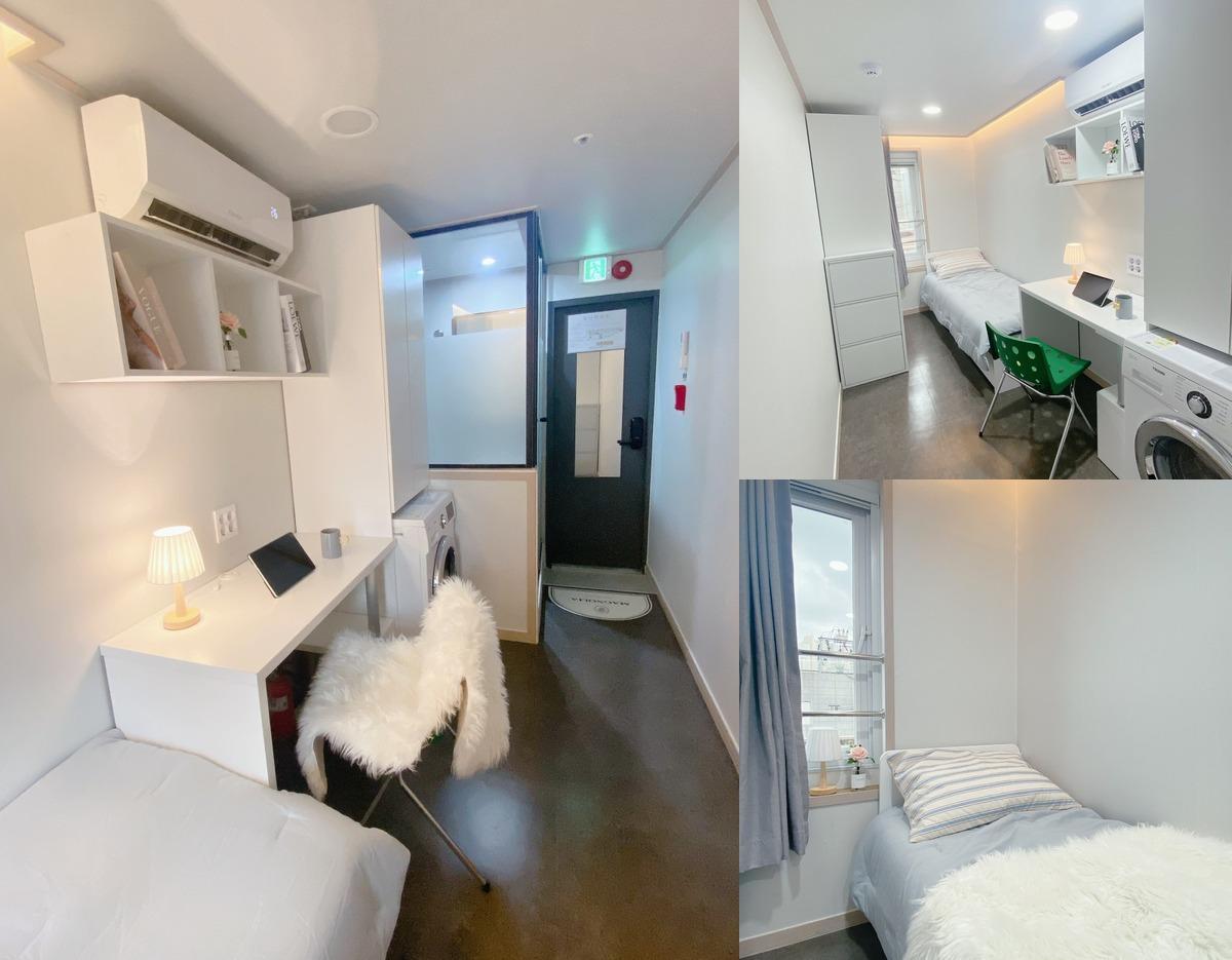 Compact all-white studio room with bed, desk, shelving, washing machine, air conditioner and narrow entry corridor.