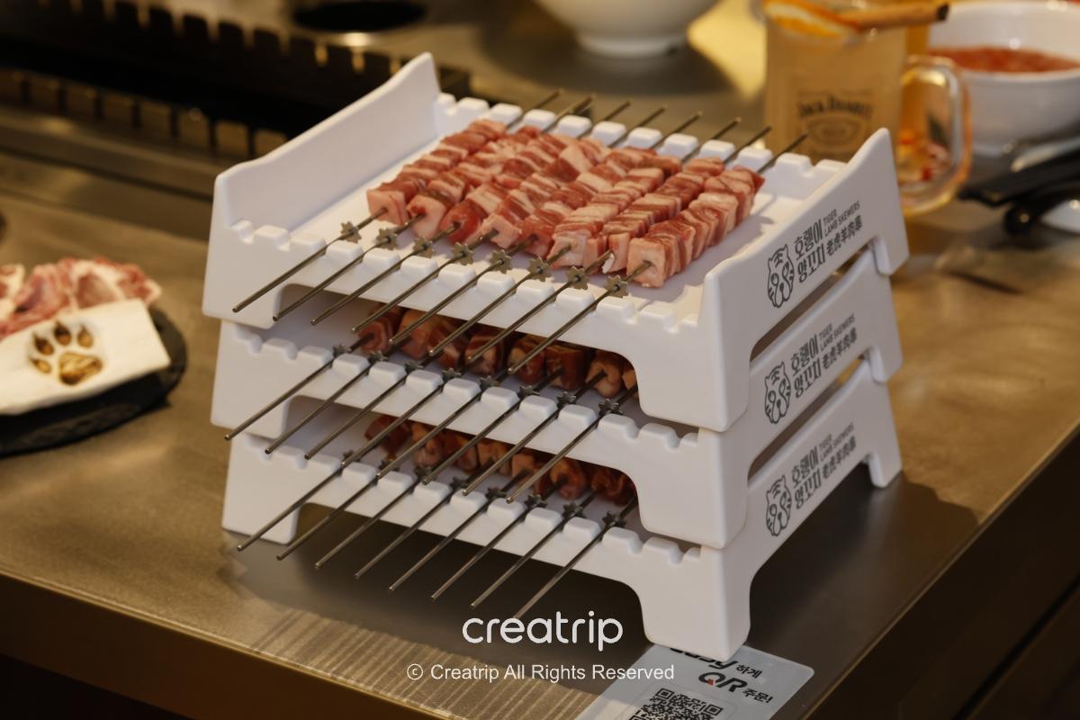 호랭이양꼬치 skewers stacked on white multi-tier rack showing raw cubed lamb belly ready for grilling with dipping sauces nearby