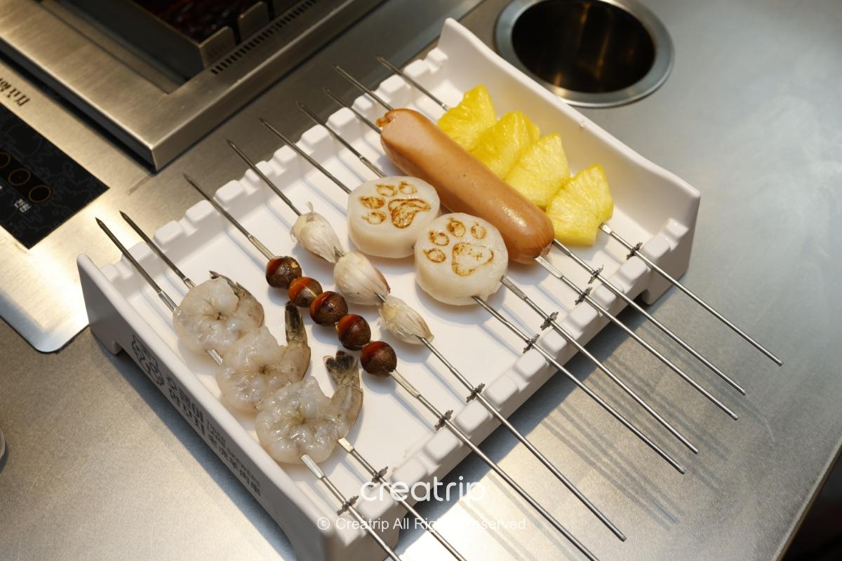 호랭이양꼬치 skewers on a tray: raw shrimp, chestnuts, garlic, stamped rice cakes, sausage and pineapple slices on metal skewers