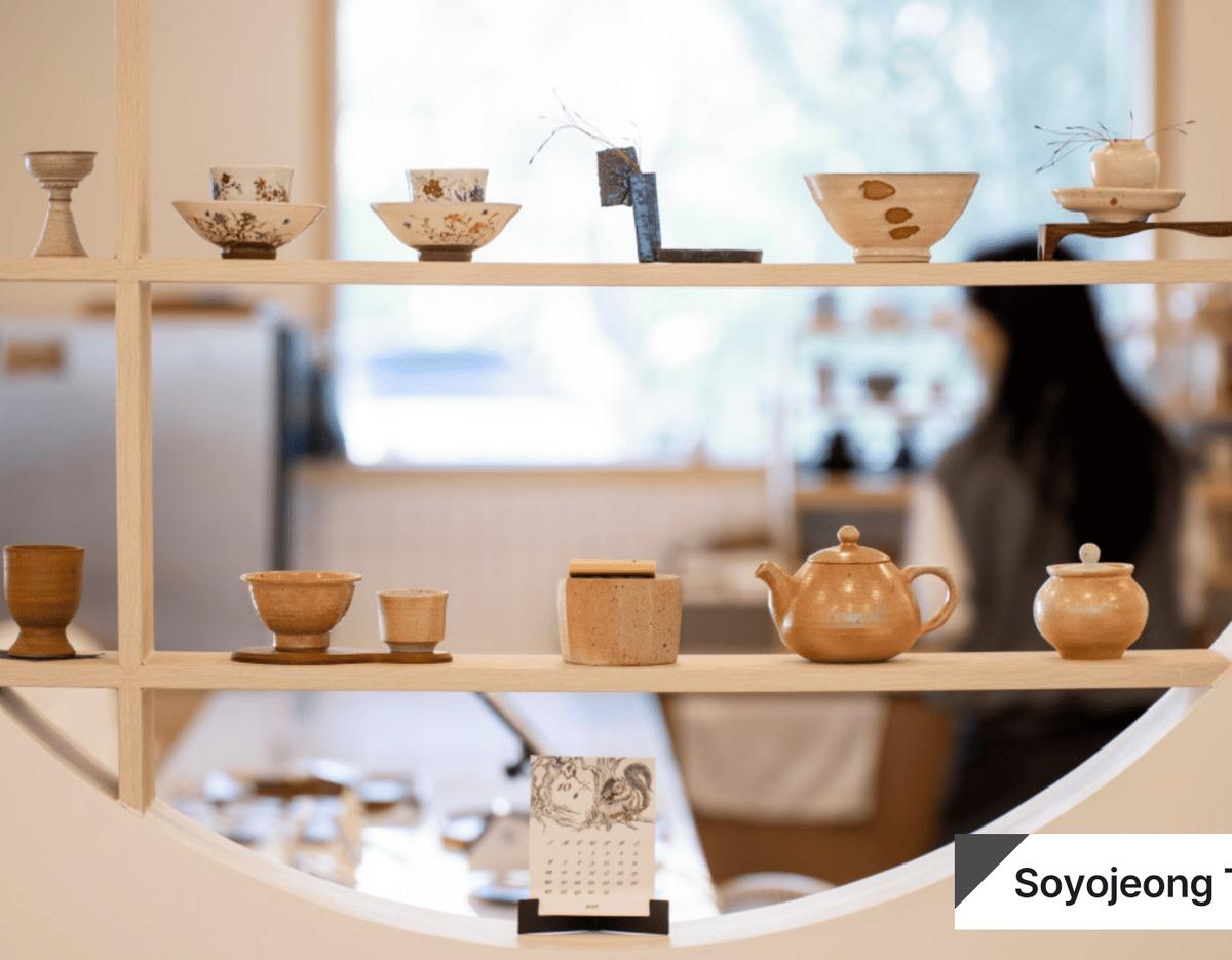 Minimal ceramic tea set and small bowls displayed on wooden shelves at Soyojeong tea cafe interior.