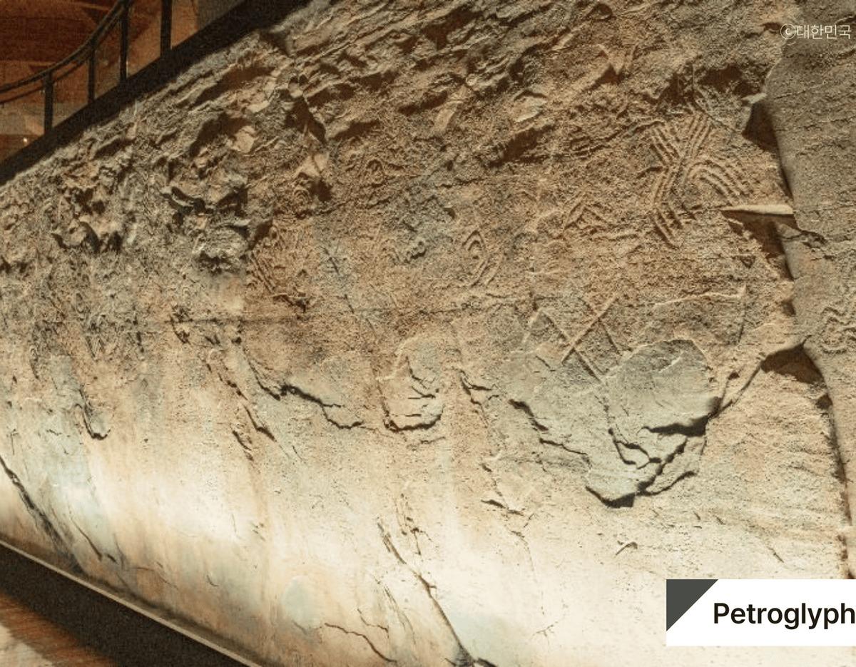 Large illuminated cliff face inside Ulsan rock art exhibit showing ancient petroglyphs and carved animal and geometric motifs