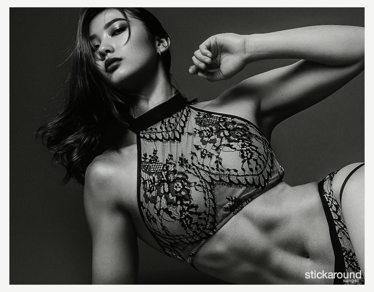 black-and-white studio portrait of a toned torso in lace high-neck bralette and matching underwear, arm raised, cropped face