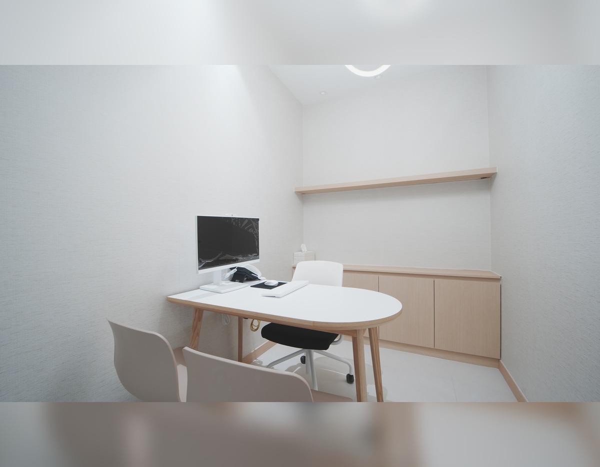 Minimal consultation room at 제이엔비의원 신사점 with white oval table, chairs, monitor, rolling chair and wood cabinets