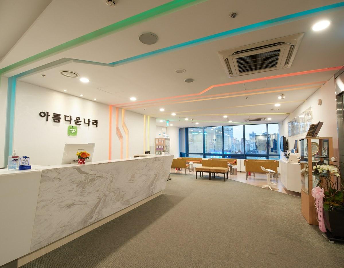 Bright modern dermatology clinic reception with marble front desk, colorful ceiling LED accents and lounge seating by large windows