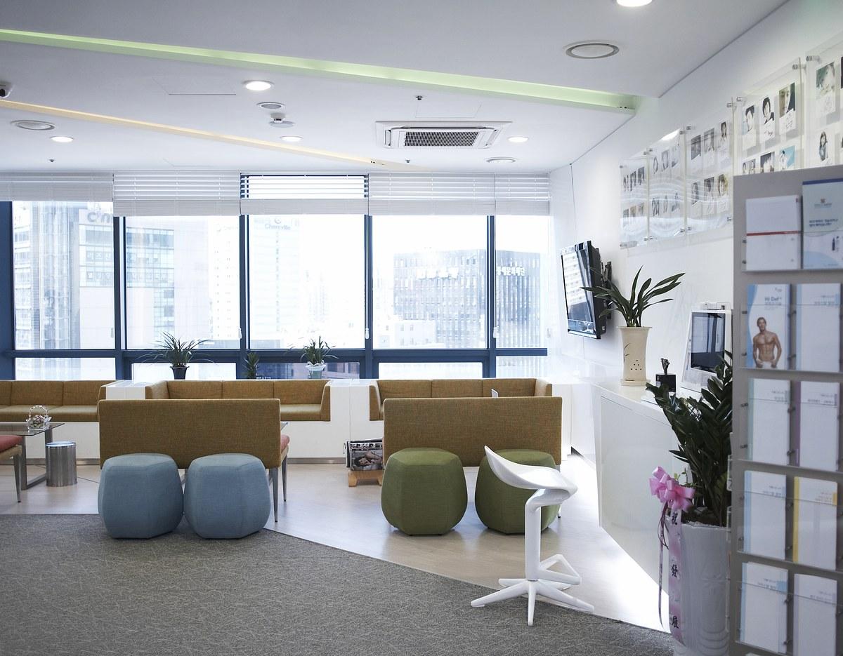 Bright clinic waiting area with sofas, round poufs, large windows overlooking city and potted plants on counters