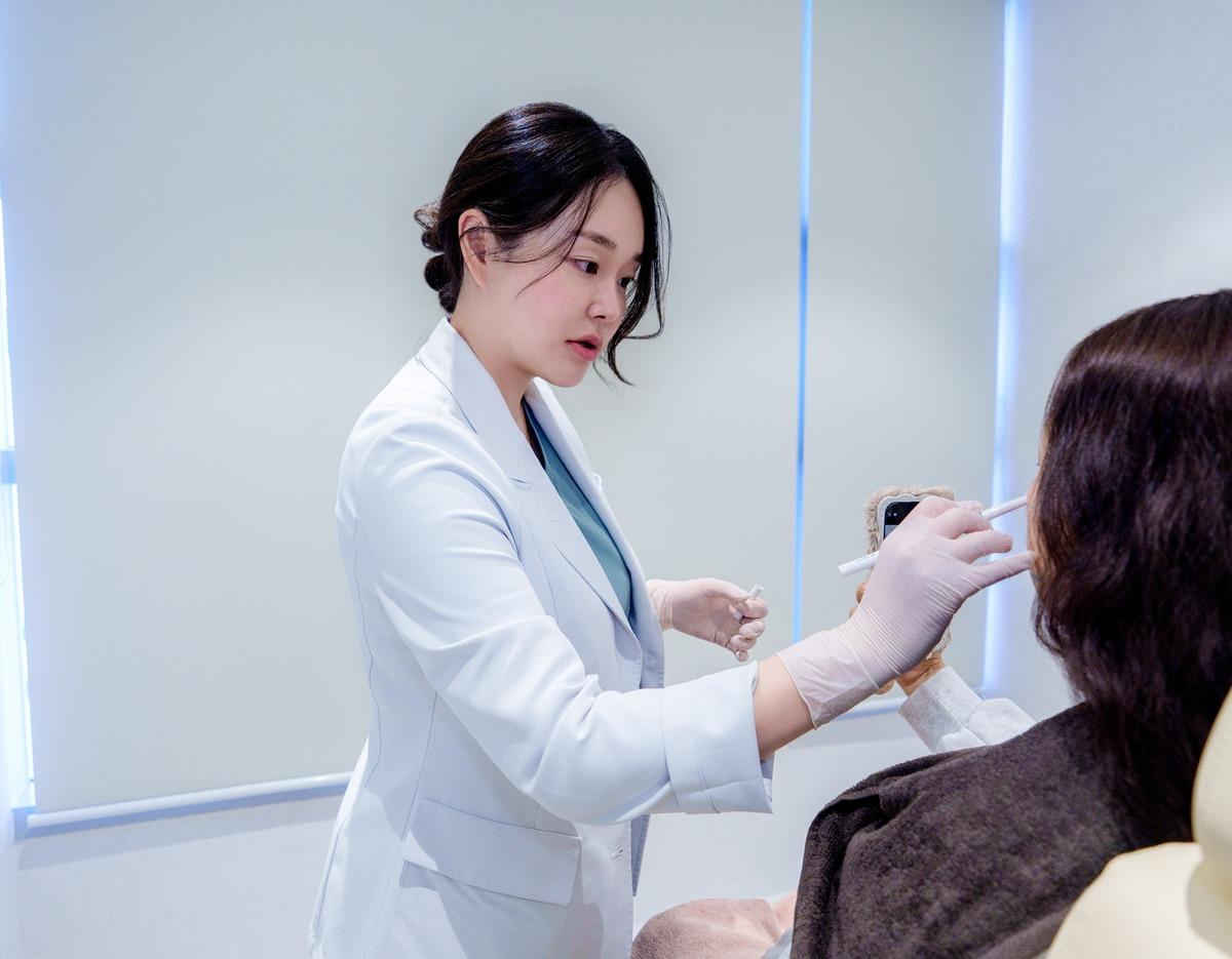 Onu Clinic practitioner in a white coat wearing gloves marking a seated patient's lips with a pen during consultation