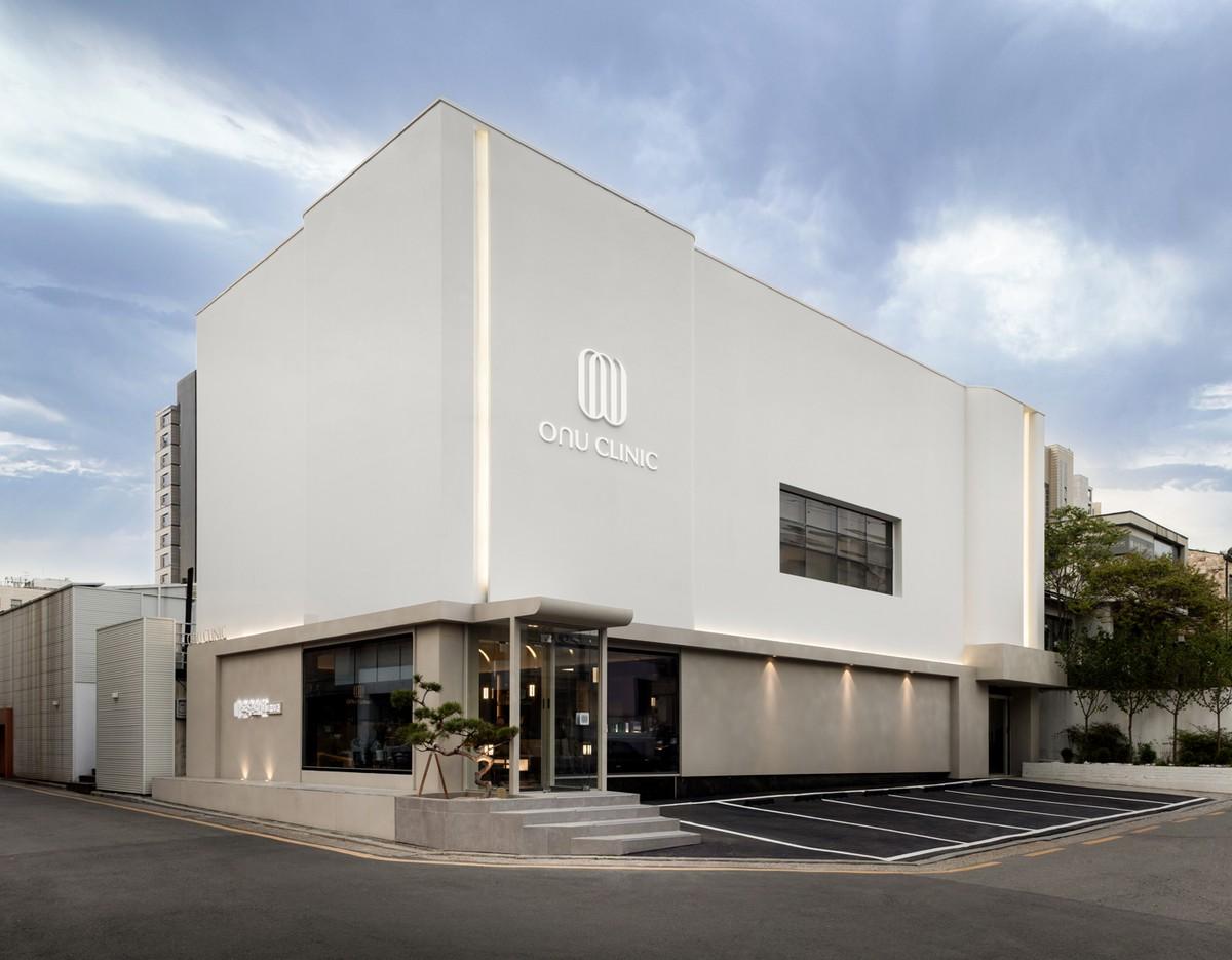 Onu Clinic modern white two-story building with minimalist facade, glass entrance and small parking area in front