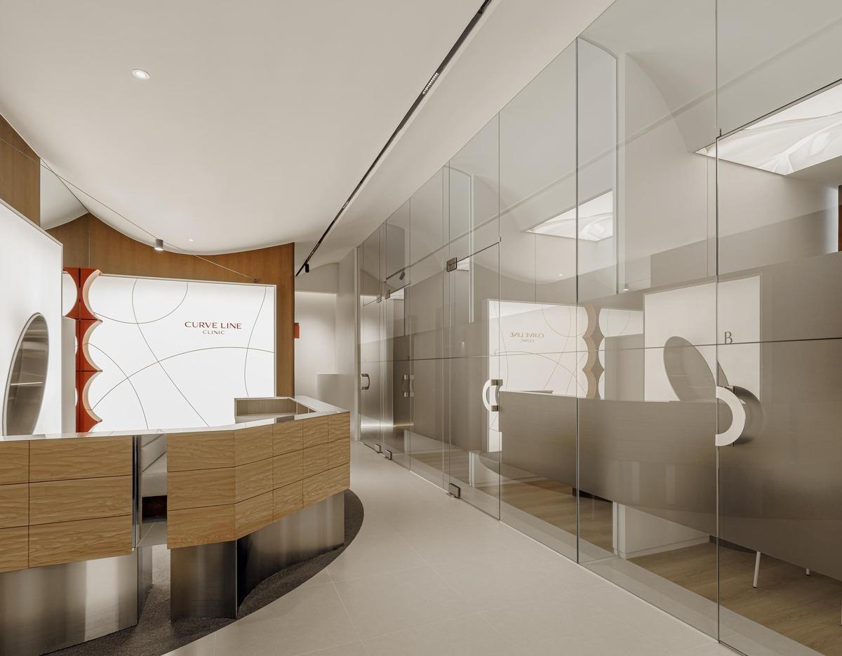 Modern clinic reception with curved wooden desk and glass-walled private treatment rooms at 커브라인의원 명동점 clinic.