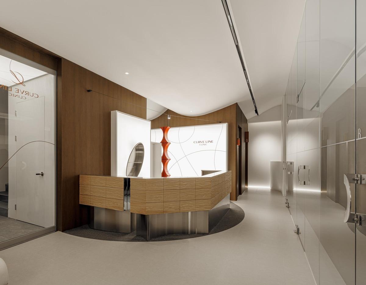 Curved wooden reception desk in a modern private clinic lobby with glass doors and backlit Curve Line Clinic sign