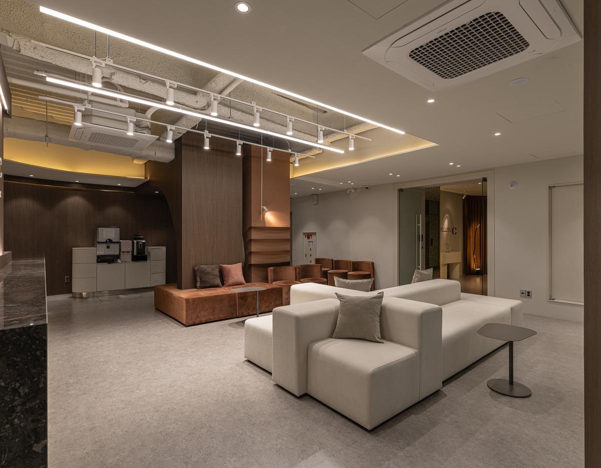 Spacious beige and brown clinic waiting area with modular sofas, accent pillows, small side tables and recessed ceiling lighting