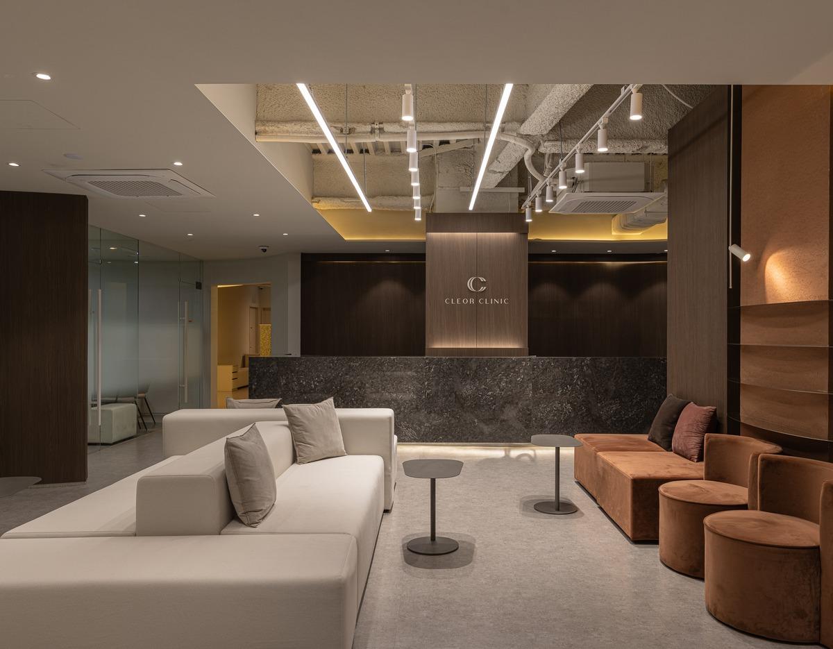 CLEOR CLINIC HONGDAE reception and lounge with beige sofa, brown velvet seating, dark marble desk, and modern lighting