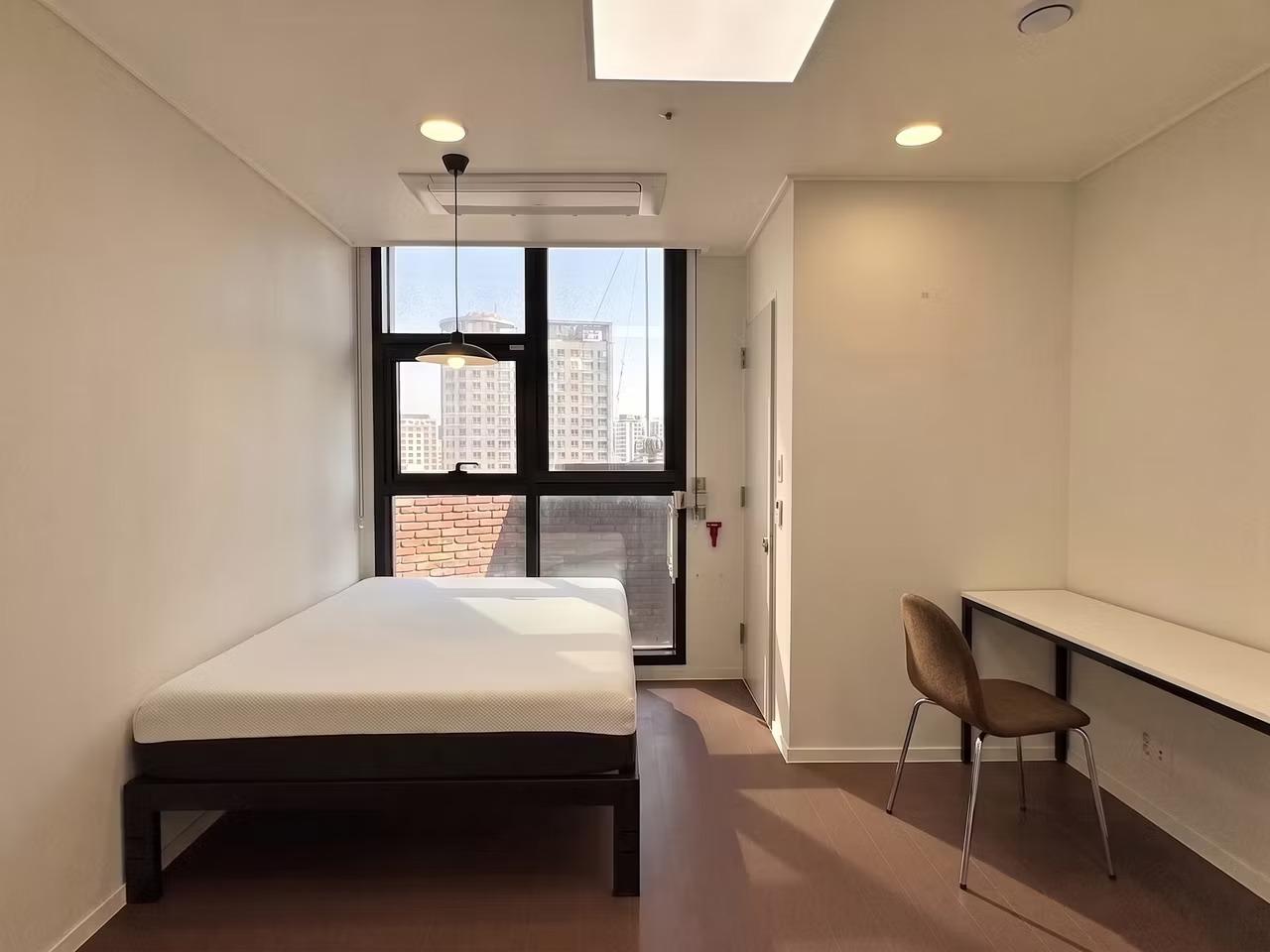 Episode Sindang studio room with single bed, desk and chair, pendant light and large window showing city view