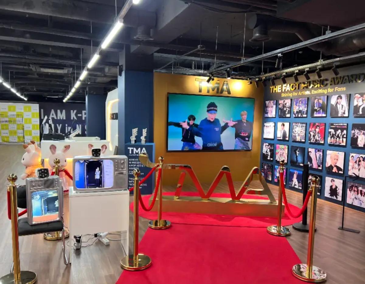 K-Culture VR Tower red carpet area with TV screens, stanchions, photo wall of K-pop artists and display props.