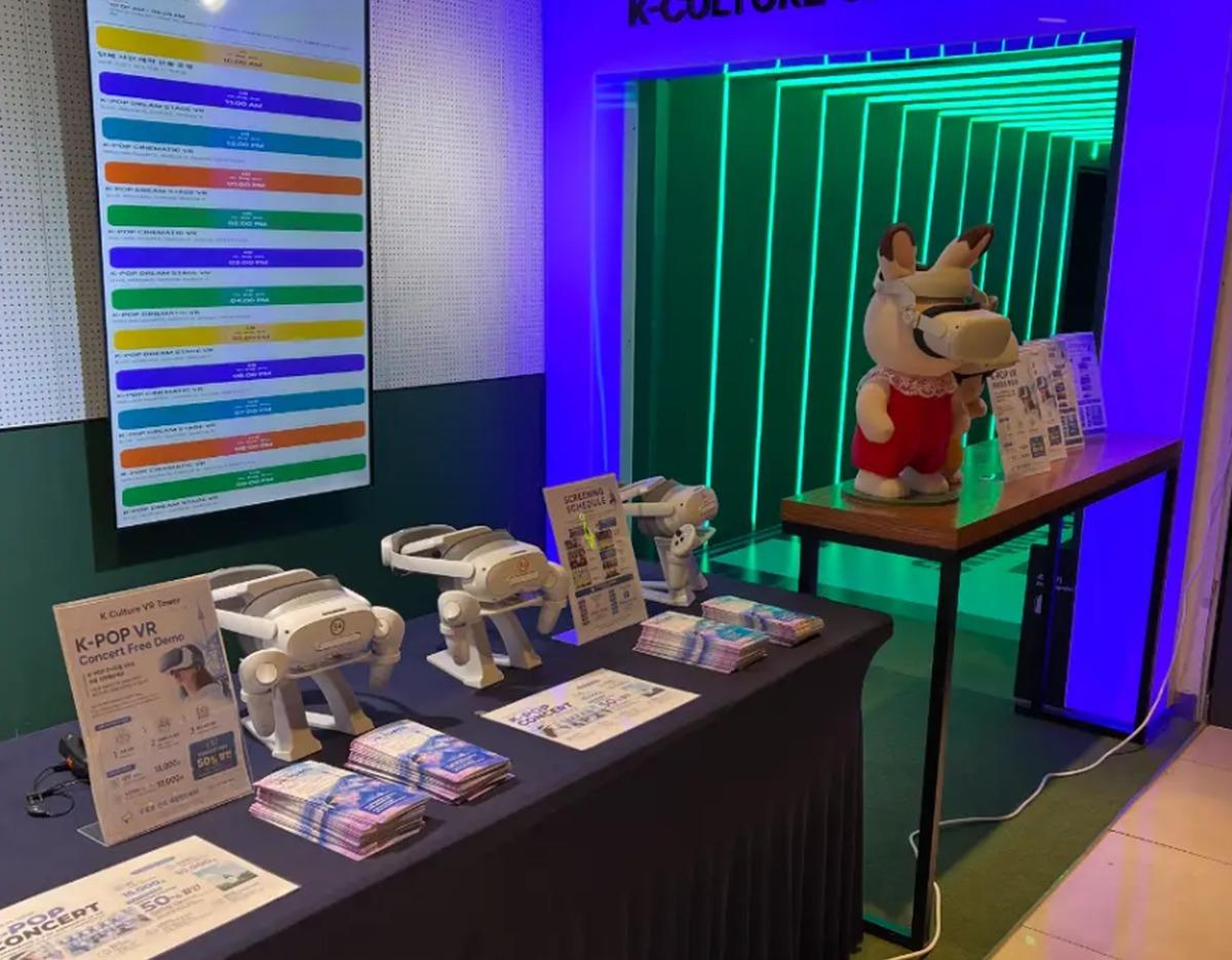 K-Culture VR Tower demo table with several 4K VR headsets, brochures, and a mascot wearing a VR headset in neon-lit entrance