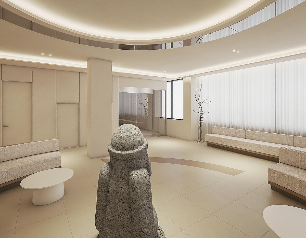 Minimalist beige waiting room with curved sofas, round tables and a stone Dol hareubang statue in center at 케이뷰티성형외과 제주점