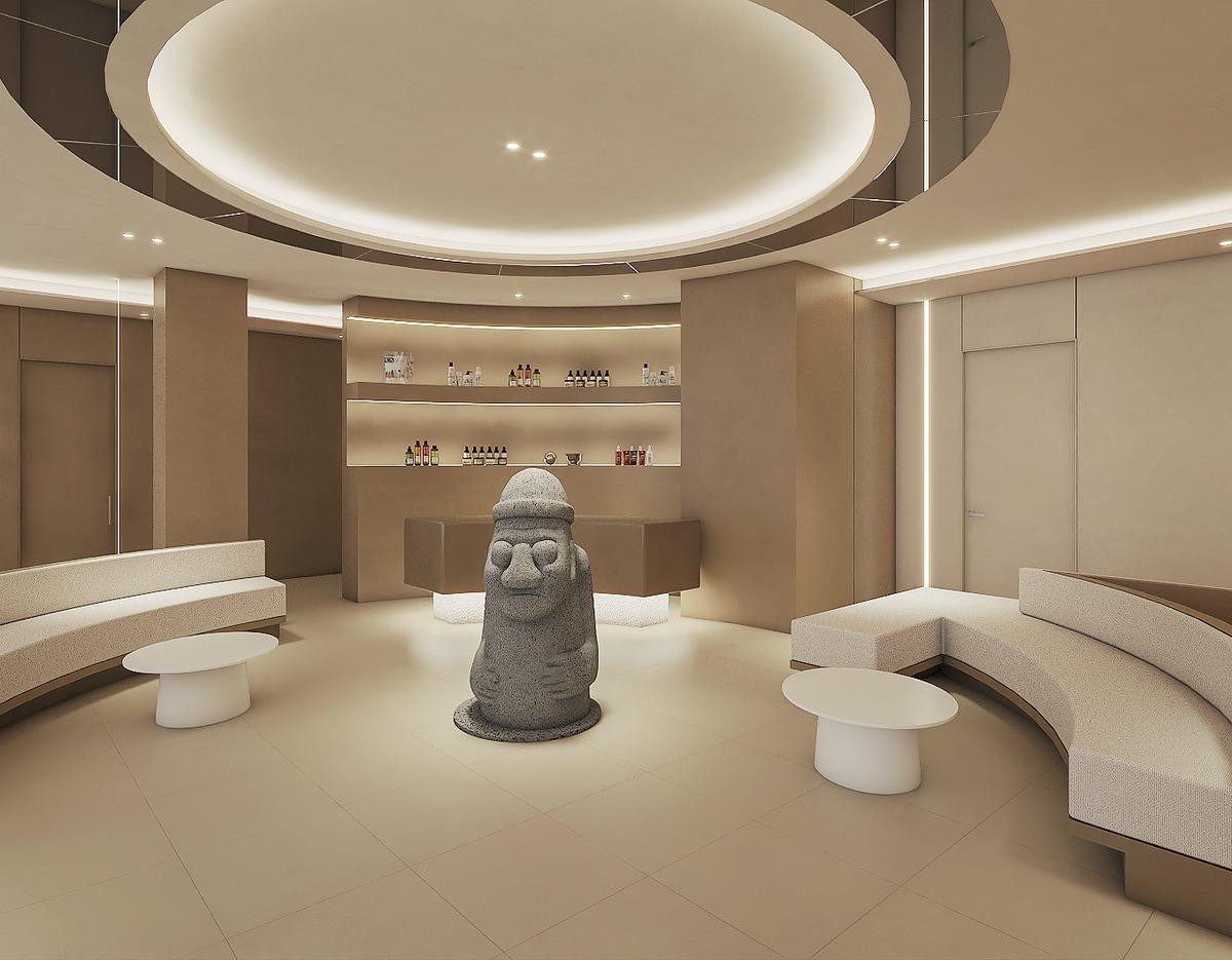 Minimalist beige clinic waiting area with curved sofas, round coffee tables, backlit display shelves and a central Jeju dol hareubang statue.