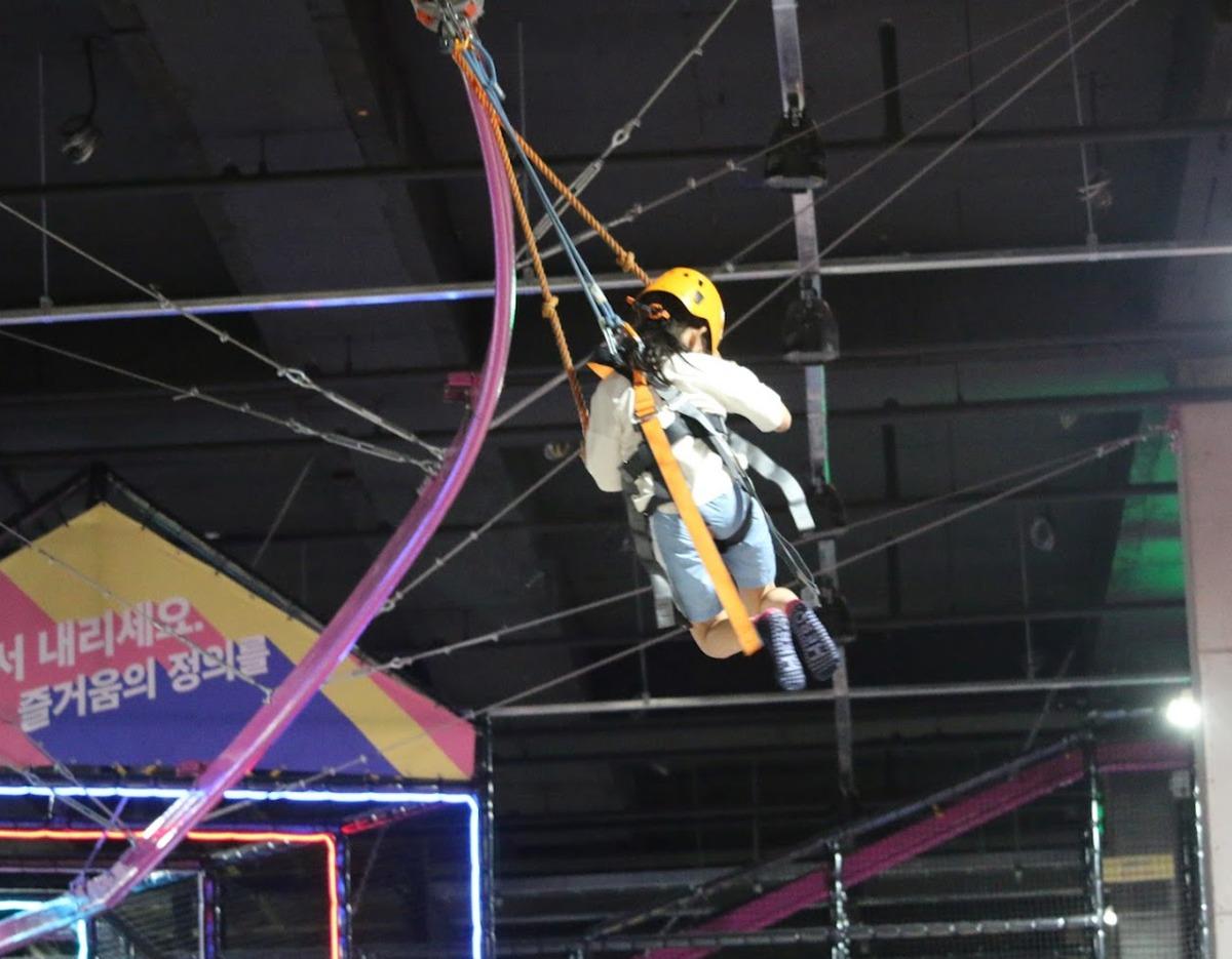 Jeju Bounce Superpark indoor zip coaster rider suspended by harness and helmet on an overhead track in activity zone