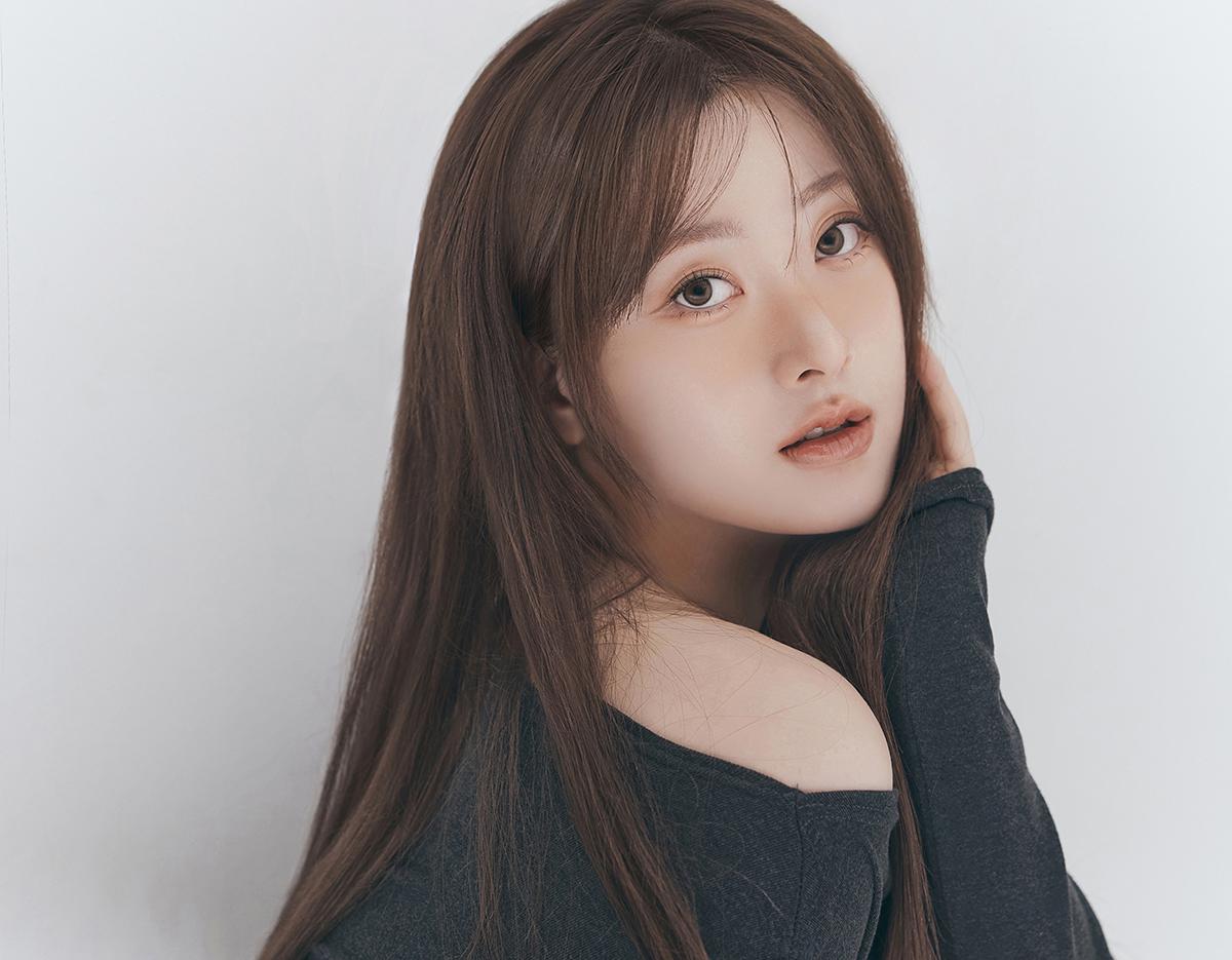 young woman with long brown hair looking over shoulder, bare shoulder showing, neutral studio background