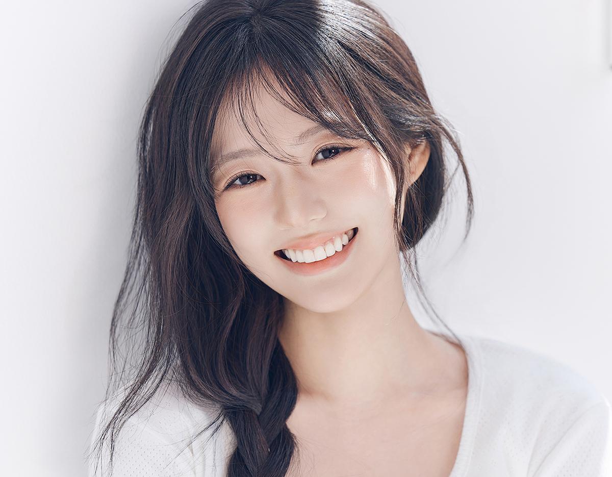 Young woman with long dark hair and soft bangs smiling warmly in a bright studio headshot for K-profile photography.