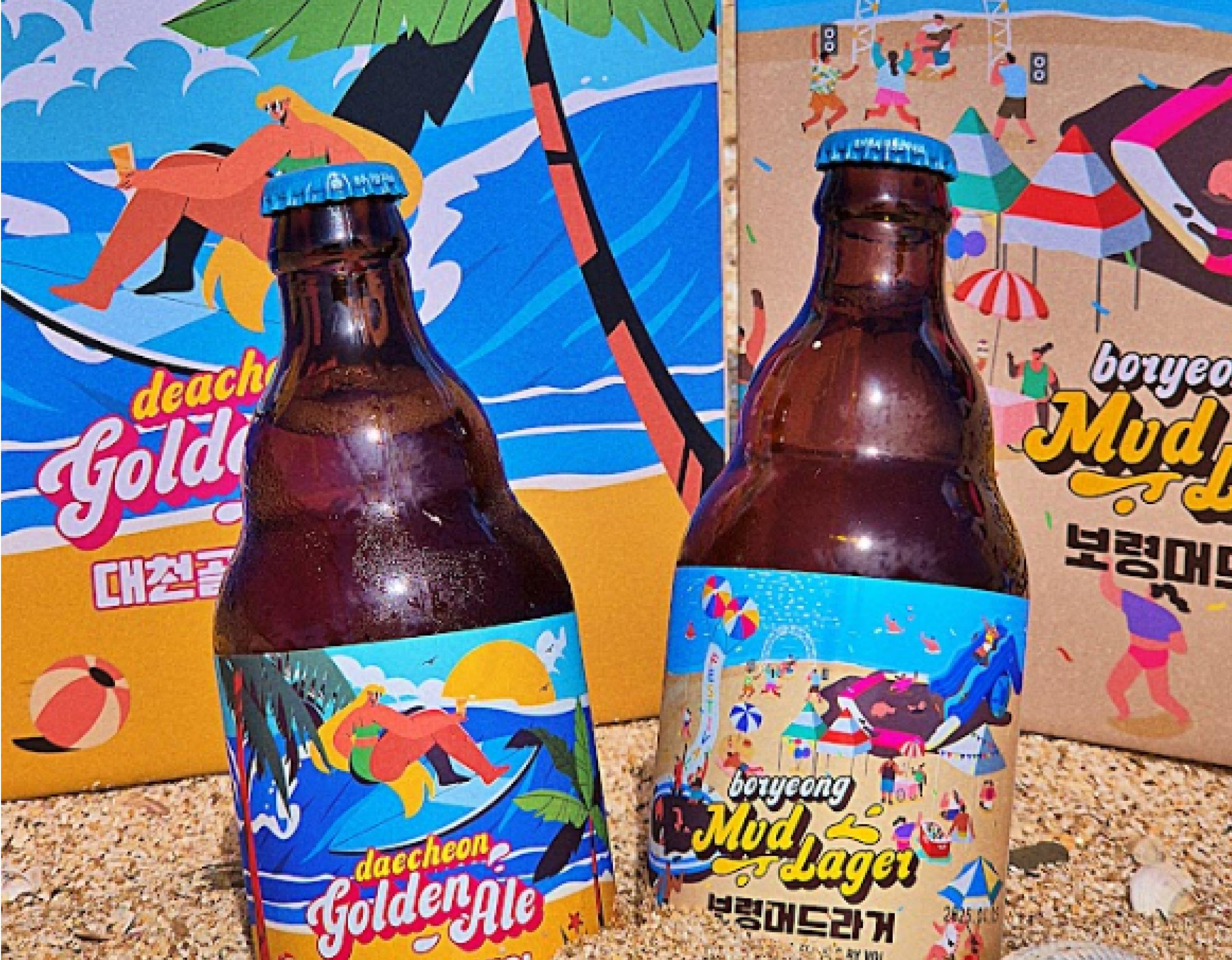 two brown beer bottles with colorful seaside labels showing surfers, palm trees and beach festival artwork on sand background