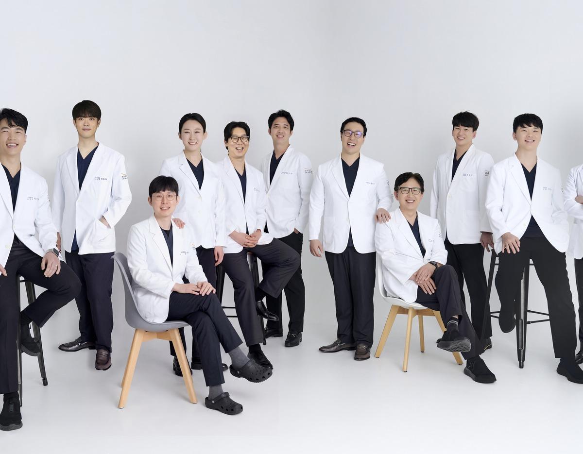 Group portrait of ten Yonsei Heal Dental Clinic doctors wearing white coats, seated and standing against a white studio background