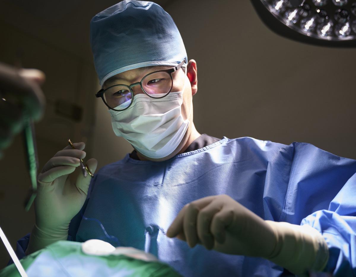 Dentist in surgical cap, mask and gloves performing a dental procedure under operating light at Yonsei Heal Dental Clinic.