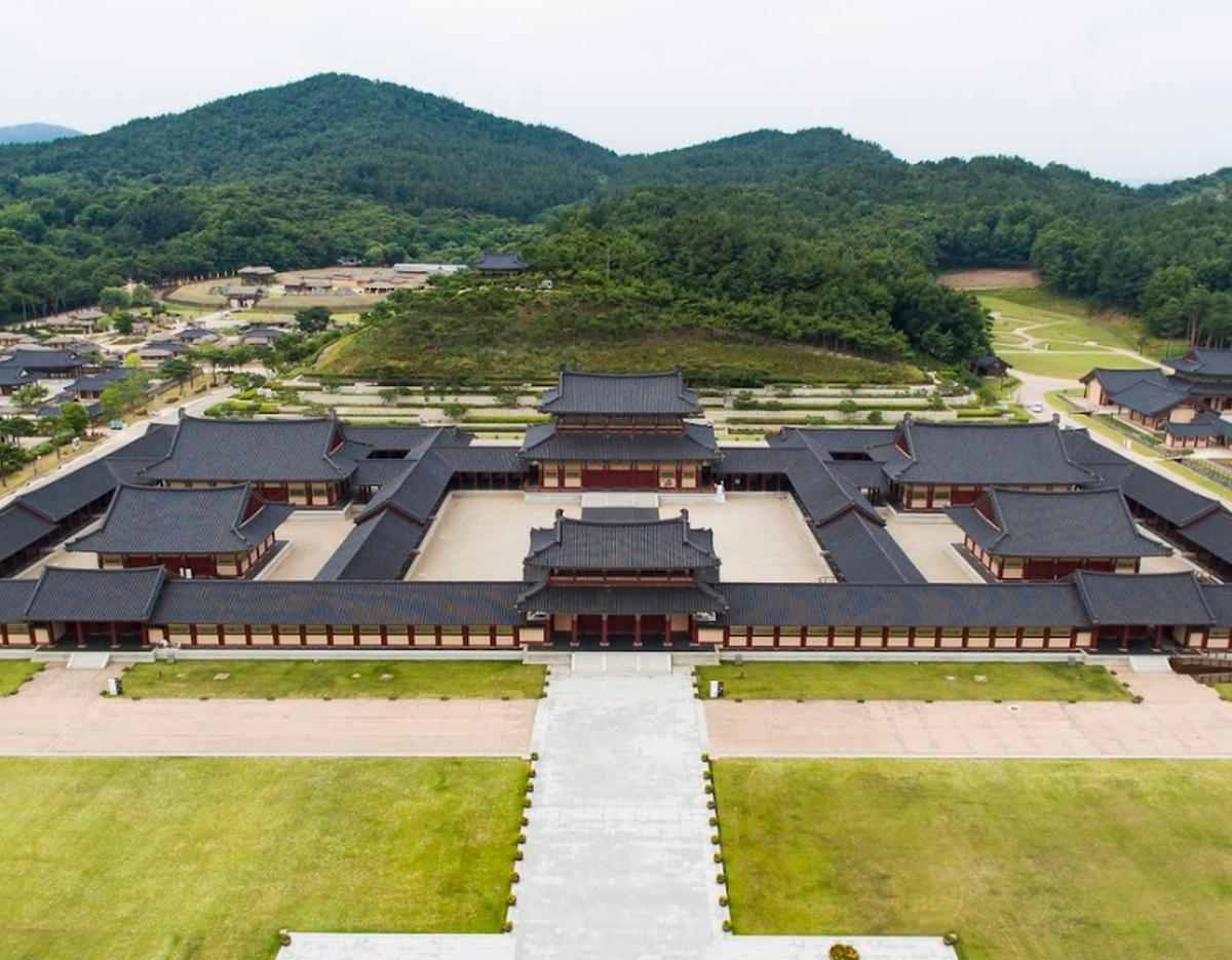 Aerial view of a large traditional Korean palace complex with tiled roofs, courtyards and surrounding wooded hills (Chungnam Tourpass).